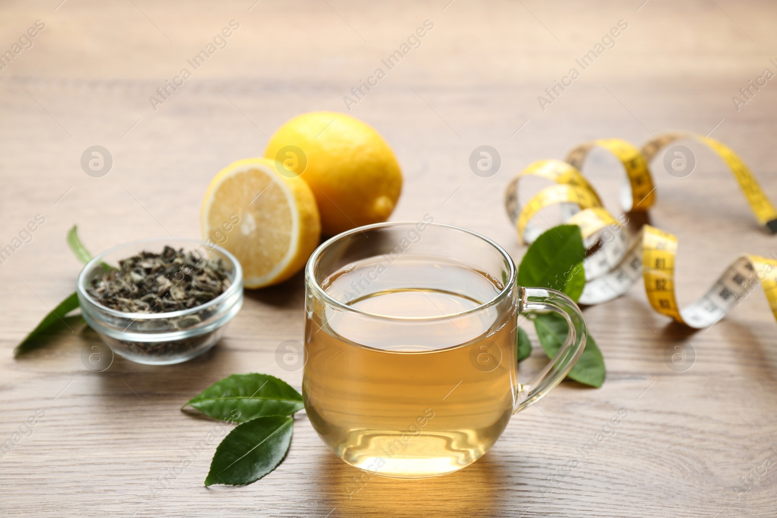 Photo of Herbal diet tea, lemon and measuring tape on wooden table