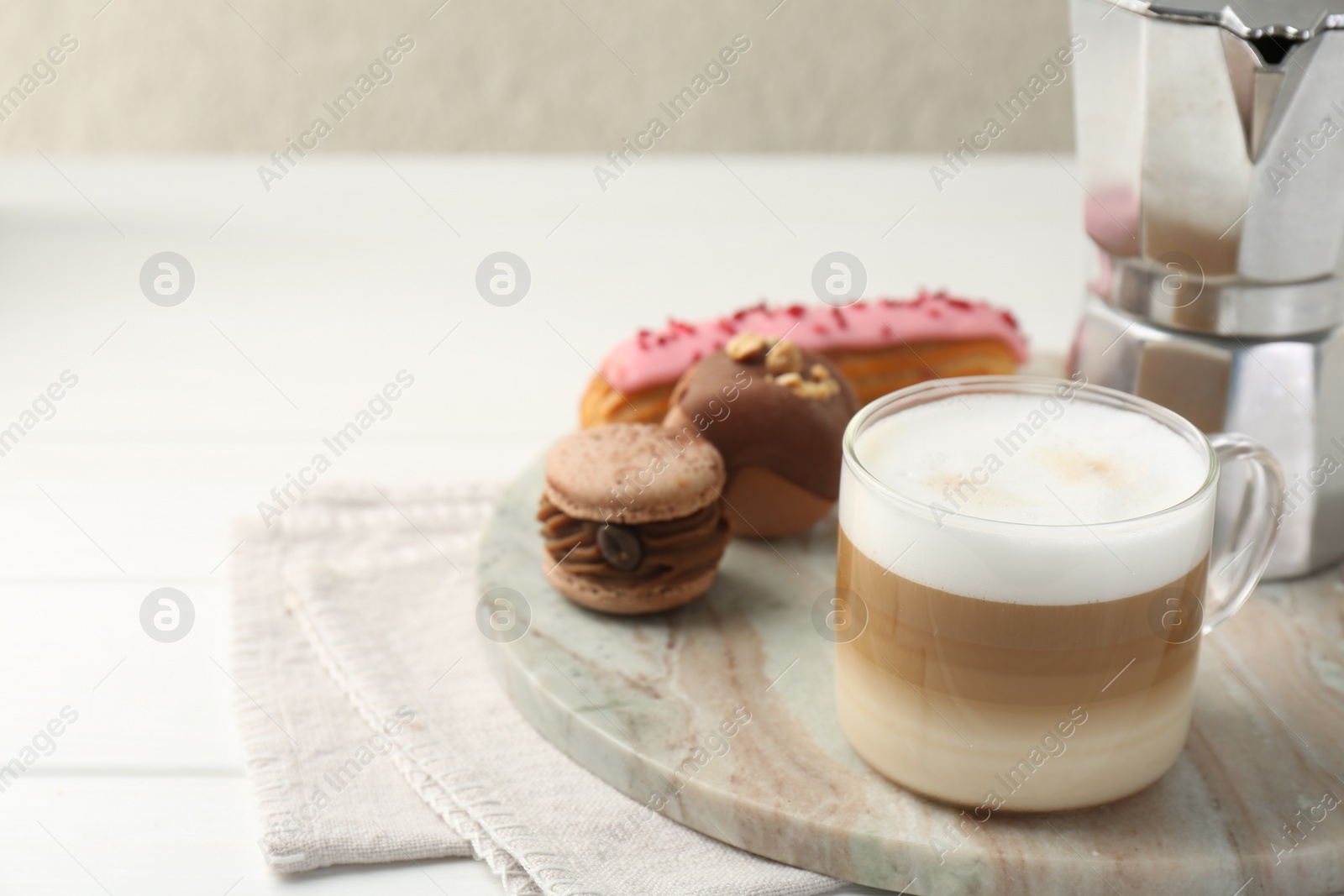 Photo of Aromatic coffee in cup, tasty macarons, eclair and moka pot on white wooden table, space for text