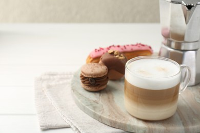 Aromatic coffee in cup, tasty macarons, eclair and moka pot on white wooden table, space for text