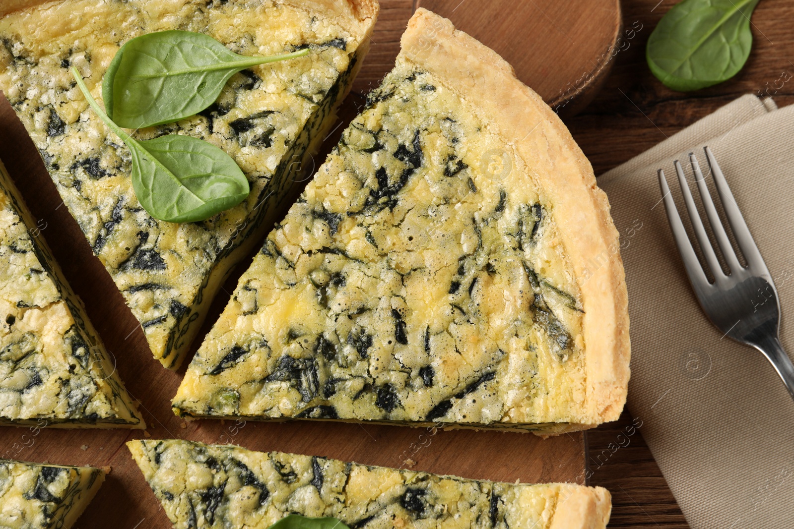 Photo of Cut delicious spinach pie with fork and napkin on table, flat lay