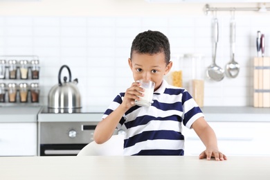 Adorable African-American boy with glass of milk in kitchen