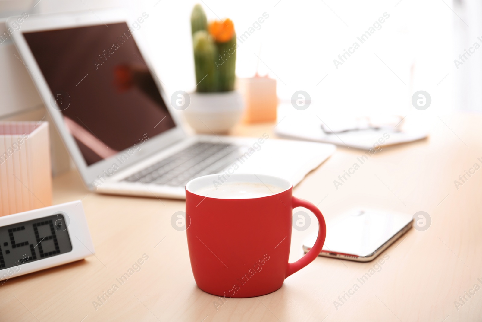 Photo of Red cup with coffee and phone near laptop on office table. Break time