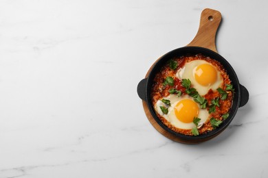 Photo of Delicious shakshuka in frying pan on white marble table, top view. Space for text