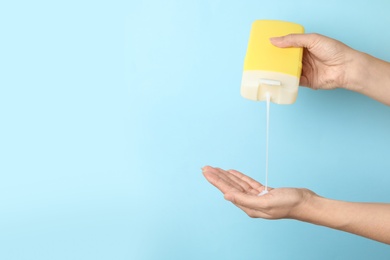 Image of Woman pouring personal hygiene product on hand against light blue background, closeup. Space for text