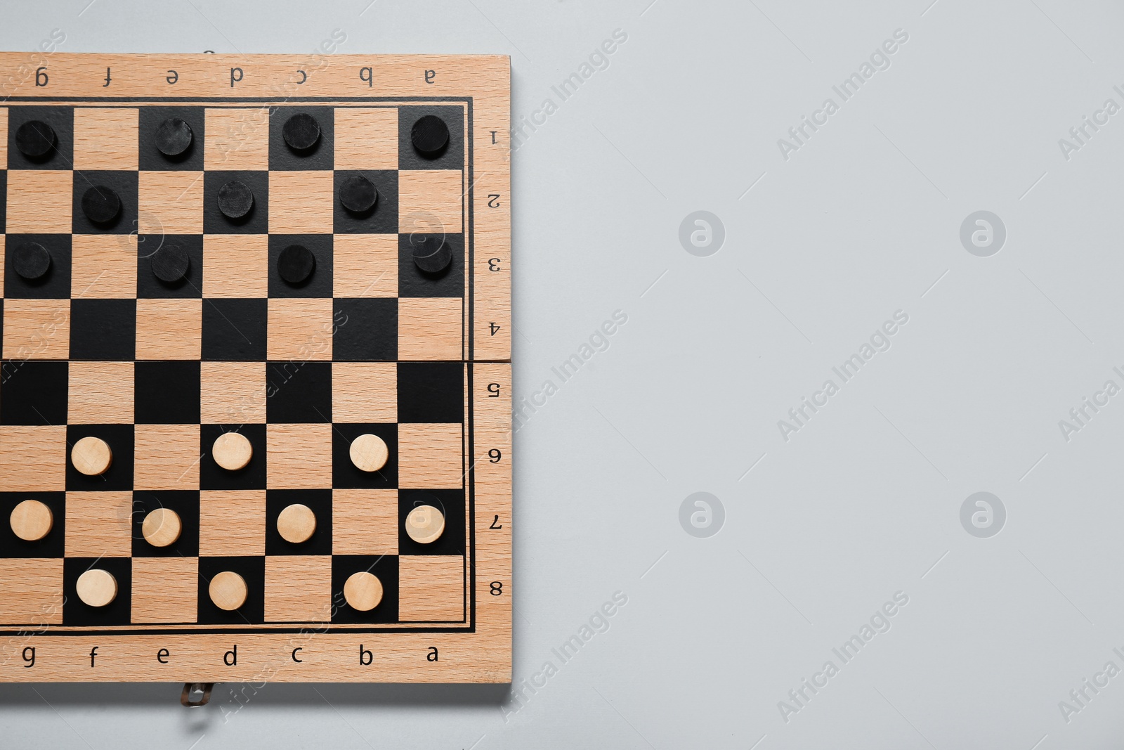 Photo of Wooden checkerboard with game pieces on light grey background, top view. Space for text