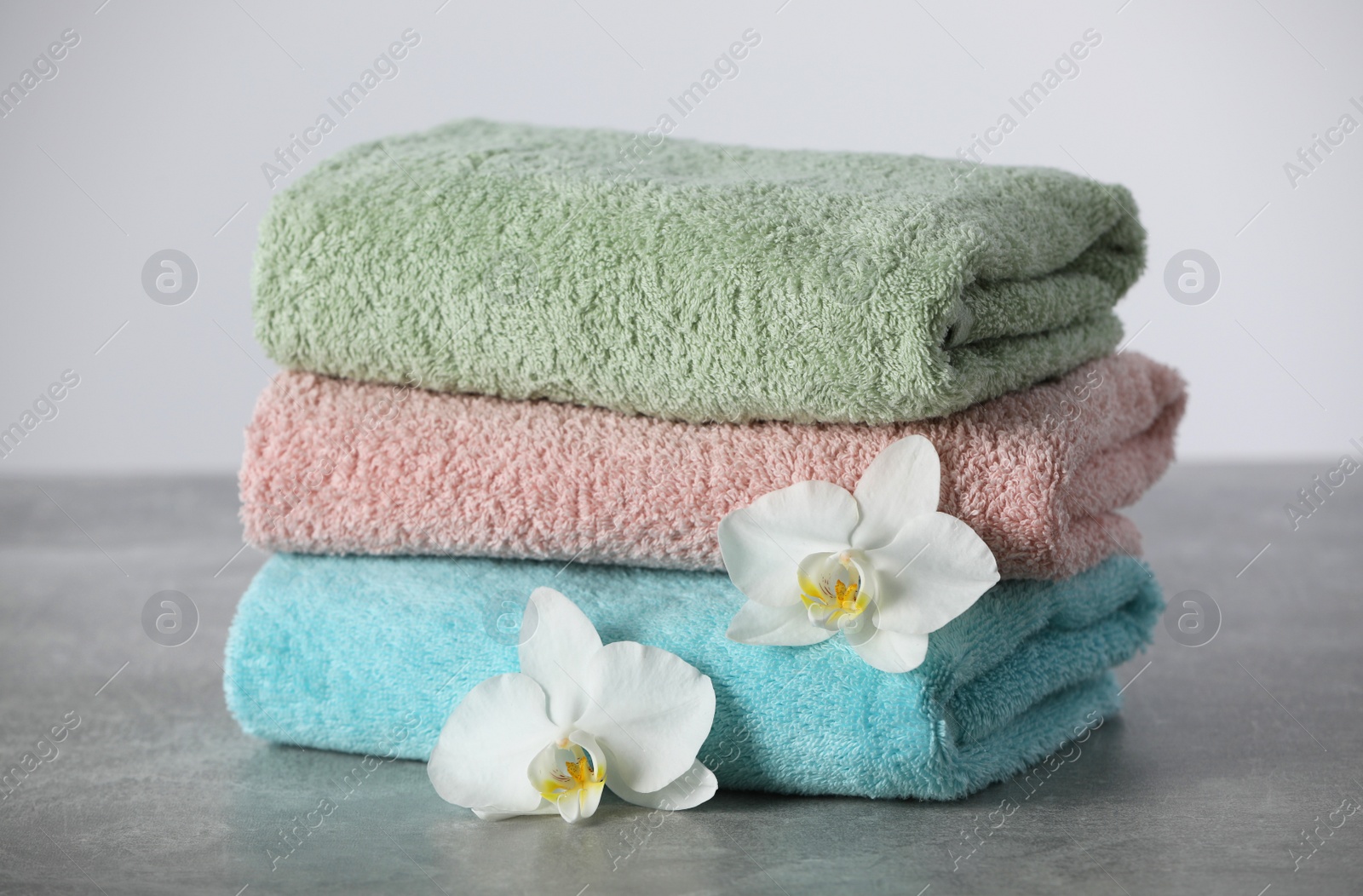 Photo of Stacked soft colorful towels with flowers on grey table