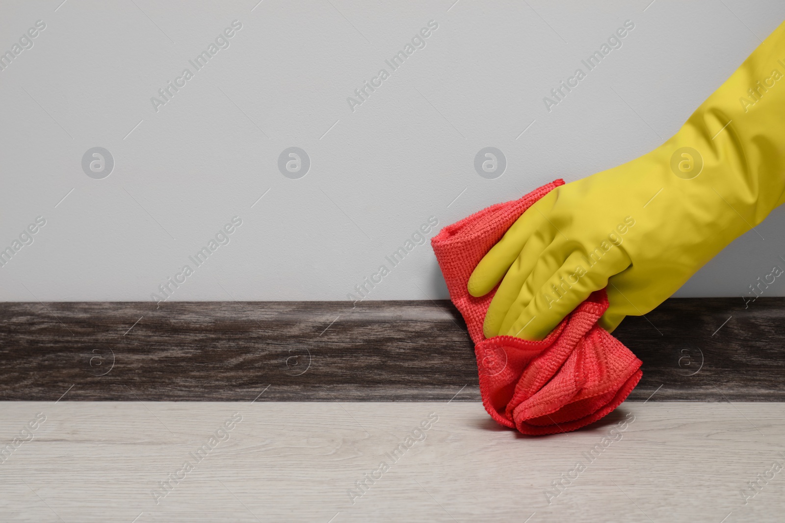 Photo of Woman in gloves cleaning plinth with cloth indoors, closeup. Space for text