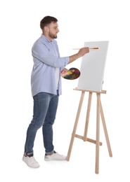 Photo of Man painting with brush on easel against white background. Young artist