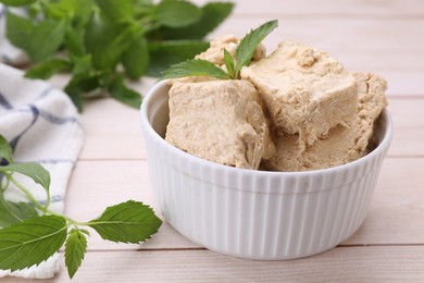 Photo of Bowl with pieces of tasty halva and mint leaves on light wooden table, closeup