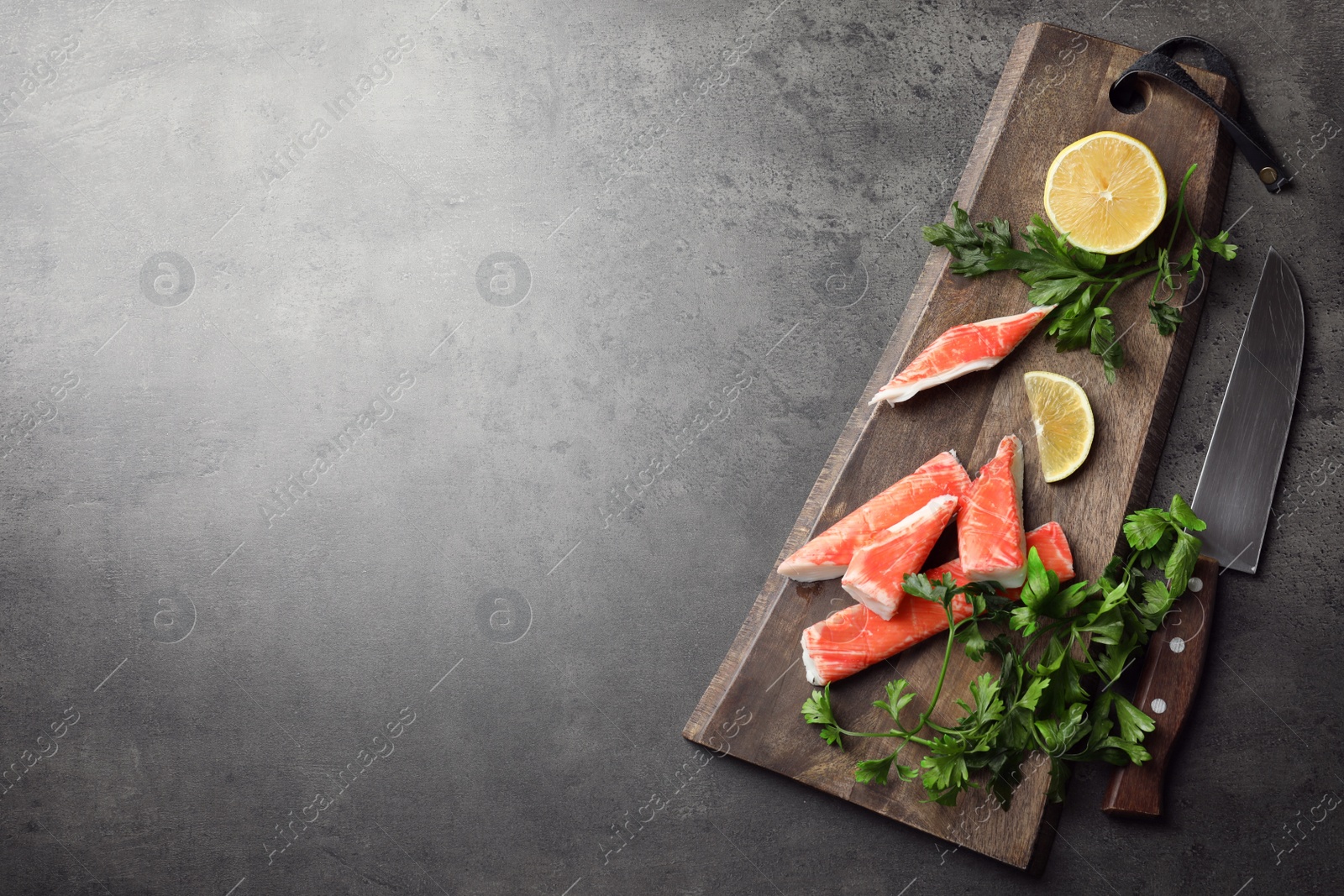 Photo of Cut crab sticks, lemon and parsley on grey table, flat lay. Space for text