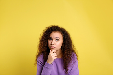 Photo of Pensive African-American woman on yellow background. Thinking about difficult question