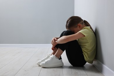Photo of Child abuse. Upset girl sitting on floor near grey wall, space for text