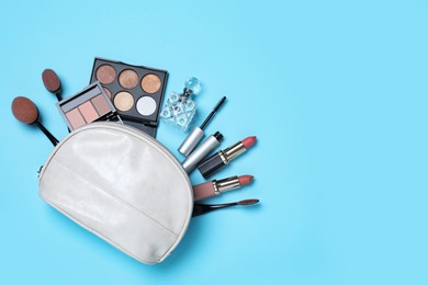 Photo of Cosmetic bag and makeup products with accessories on light blue background, flat lay. Space for text