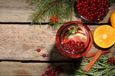 Photo of Glass bottle of aromatic punch drink, ingredients and Christmas decor on wooden table, flat lay. Space for text