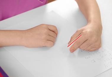 Girl erasing mistake in her homework at white desk, closeup