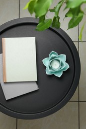 Candle in beautiful flower shaped holder and books on black table, top view