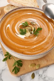 Photo of Delicious pumpkin soup served on white marble table, closeup
