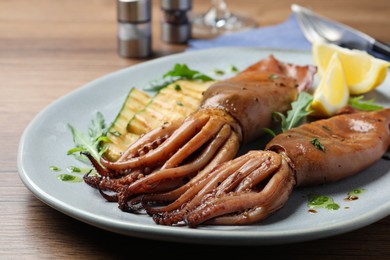 Photo of Delicious grilled squids served on wooden table, closeup