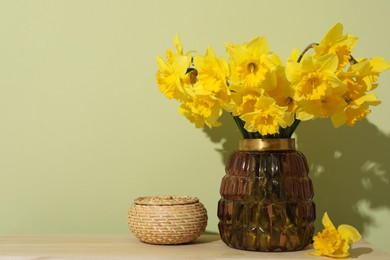 Beautiful daffodils in vase on table near light green wall, space for text