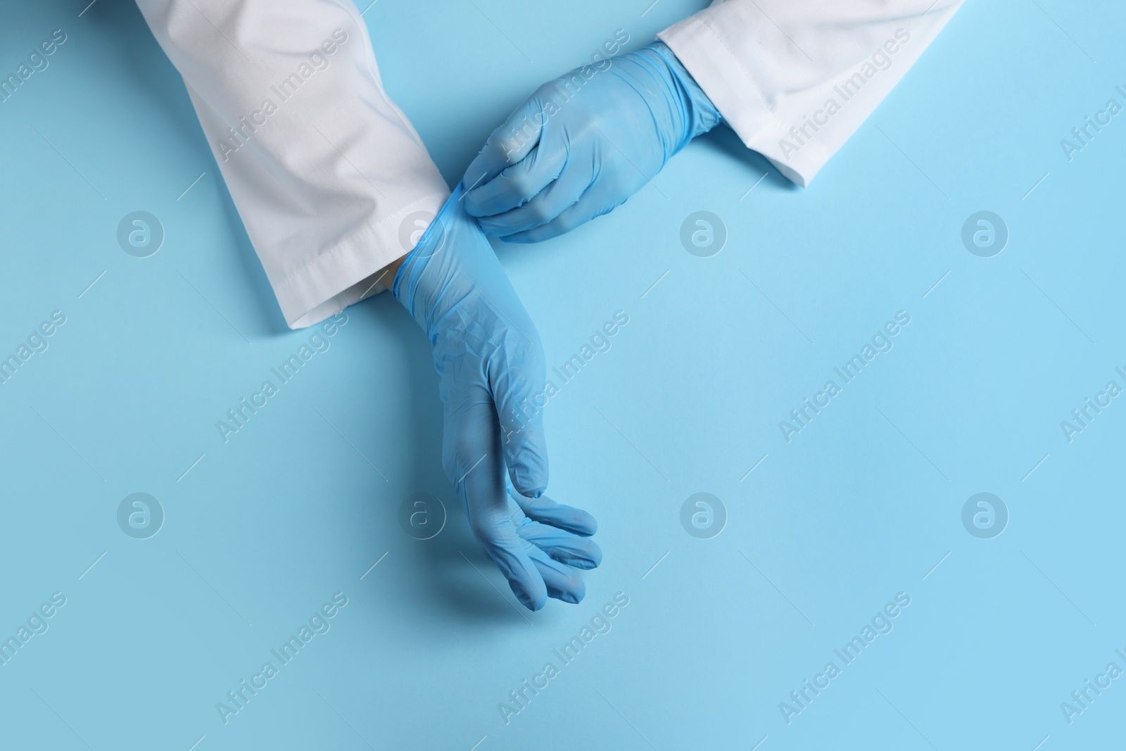 Photo of Doctor wearing medical gloves on light blue background, top view. Space for text