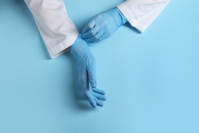 Doctor wearing medical gloves on light blue background, top view. Space for text