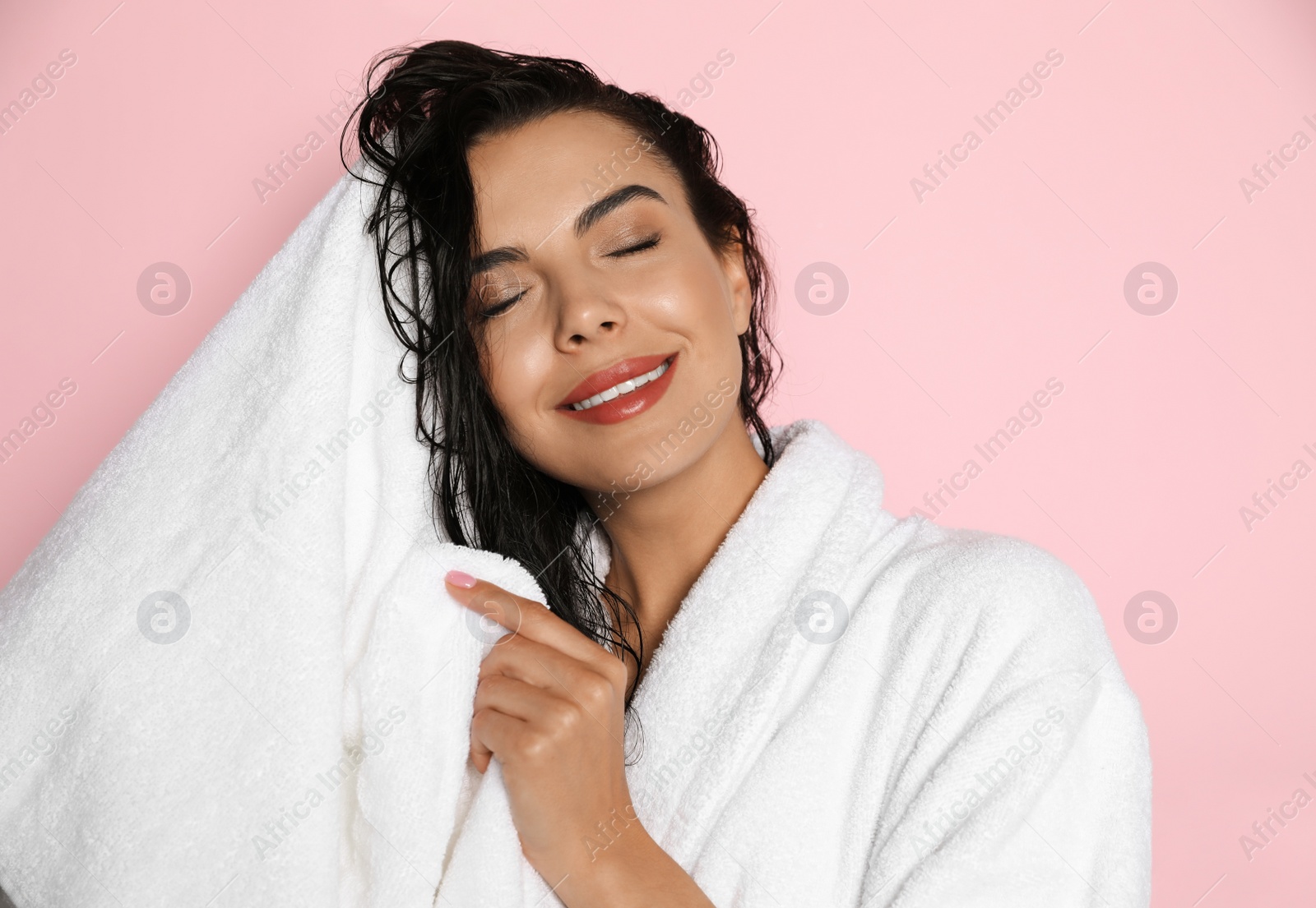 Photo of Beautiful young woman in bathrobe drying hair with towel on pink background