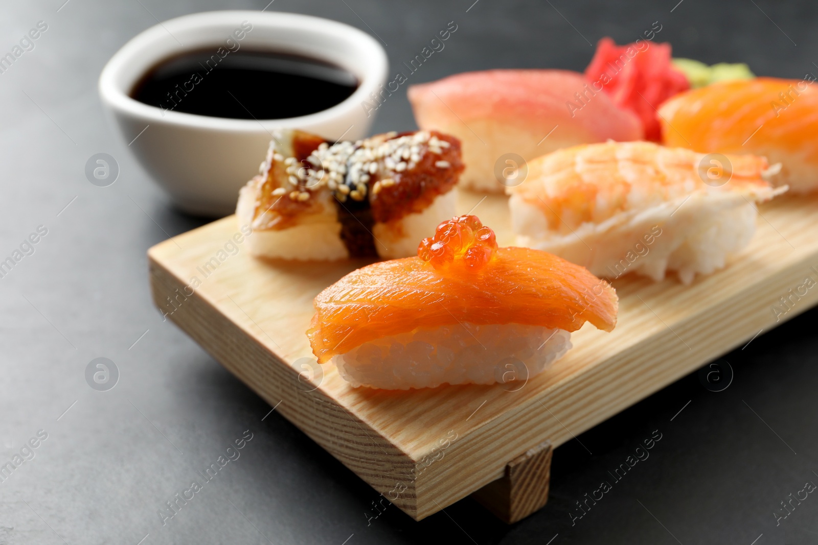 Photo of Wooden board with delicious nigiri sushi and soy sauce on black table, closeup