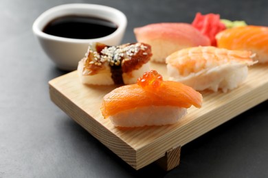 Wooden board with delicious nigiri sushi and soy sauce on black table, closeup