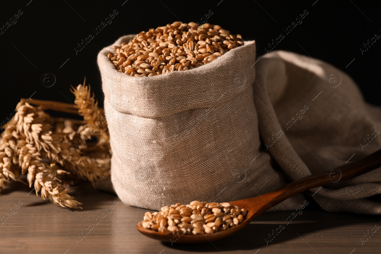 Photo of Wheat grains with spikelets on wooden table against black background