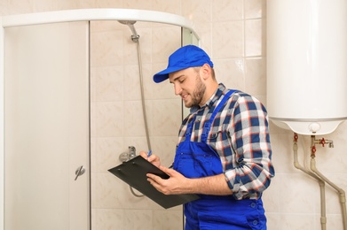 Professional plumber in uniform with clipboard indoors