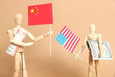 Photo of Wooden mannequins holding money, American and Chinese flags on beige background