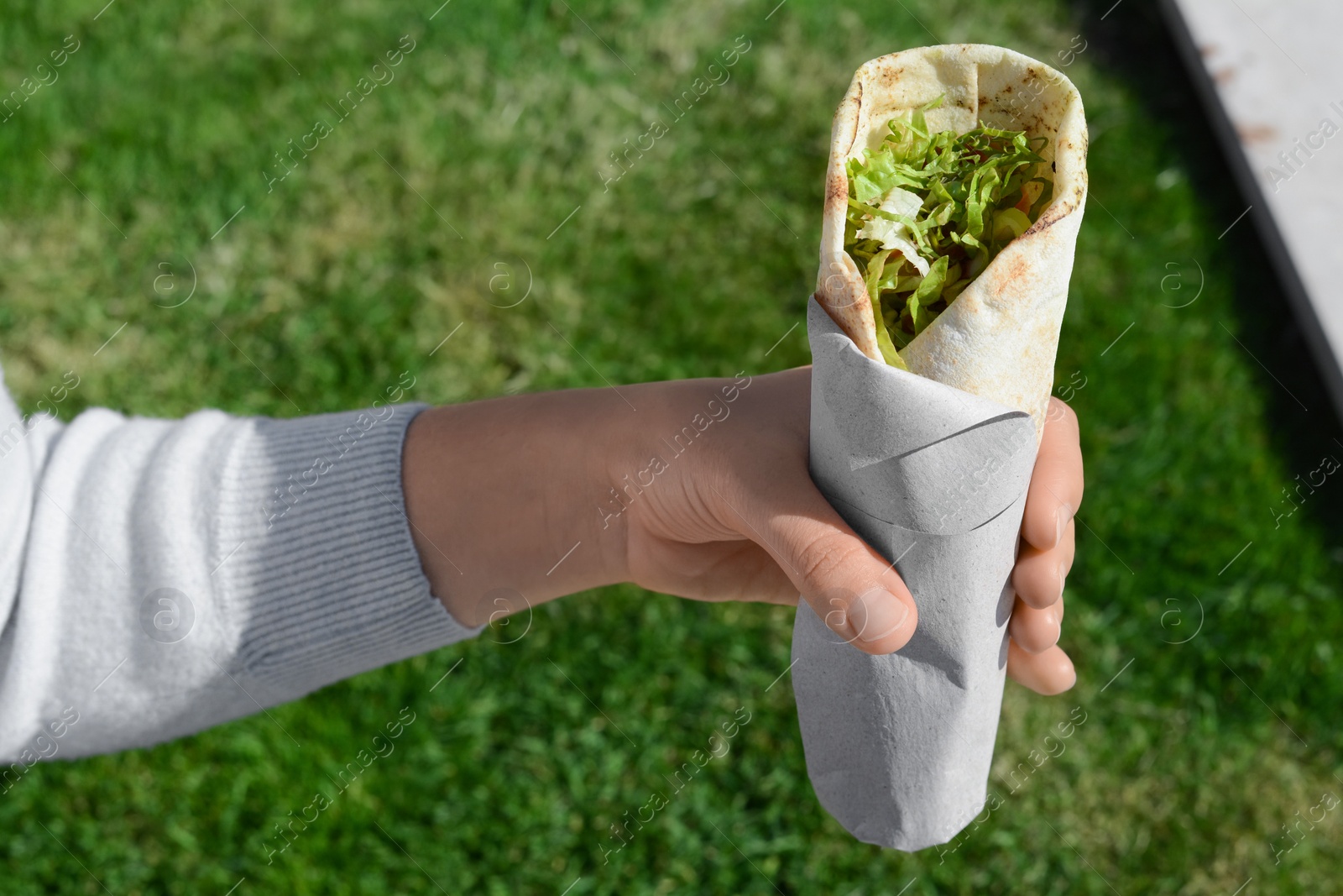 Photo of Woman holding delicious vegetable roll outdoors, closeup