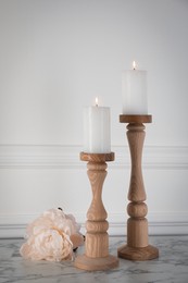 Elegant candlesticks with burning candles and flower on white marble table