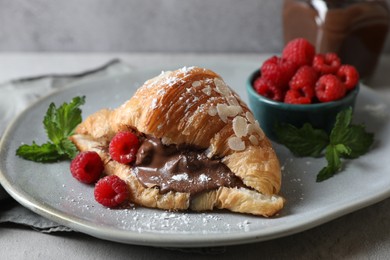 Delicious croissant with chocolate and raspberries on grey table, closeup