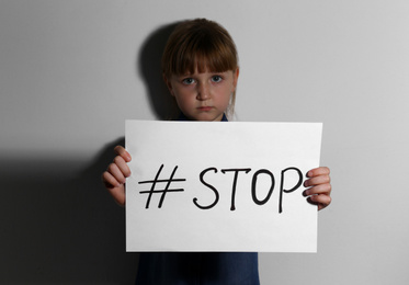 Photo of Abused little girl with hashtag STOP near white wall. Domestic violence concept