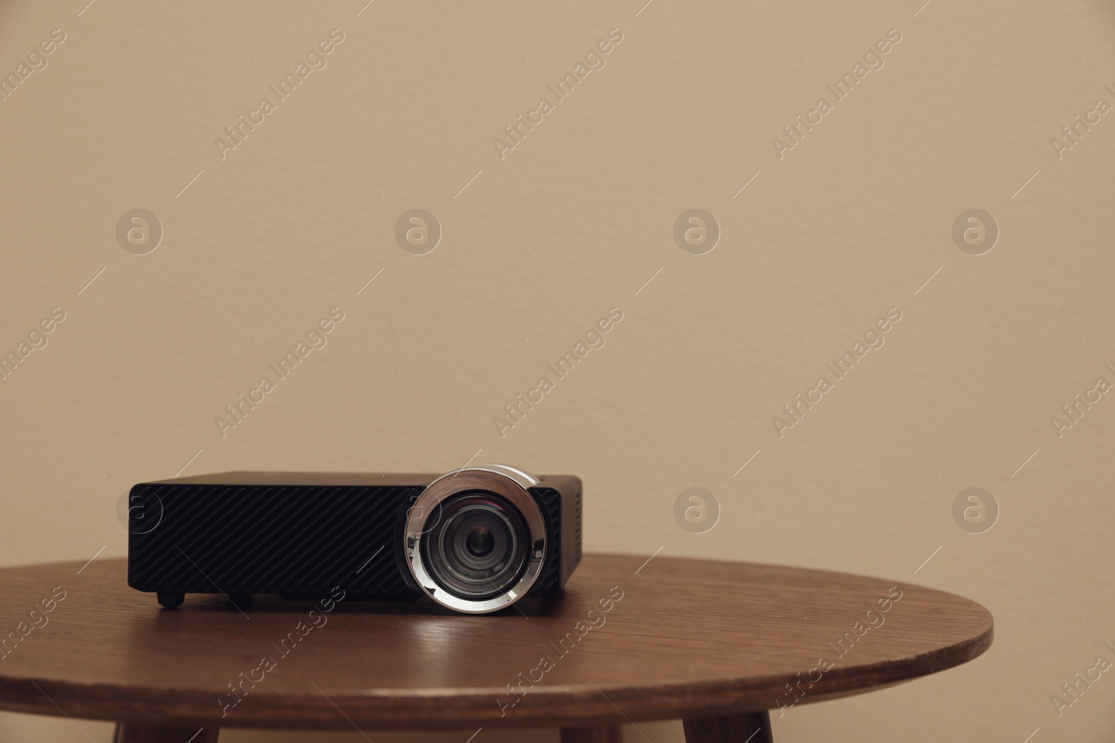 Photo of Modern video projector on wooden table against beige background. Space for text