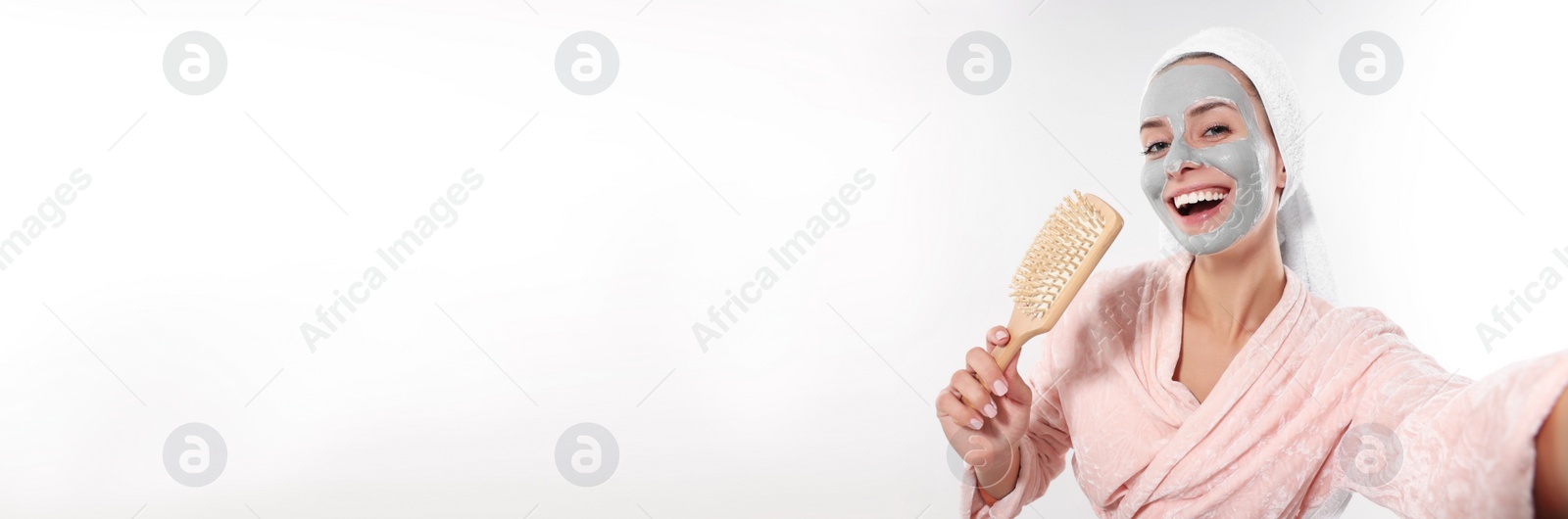 Image of Spa treatment. Happy woman with face mask and brush singing while taking selfie on white background. Banner design with space for text