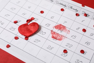 Photo of Calendar with marked Valentine's Day, confetti and heart on red background, closeup