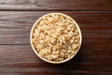 Photo of Delicious pearl barley in bowl on wooden table, top view