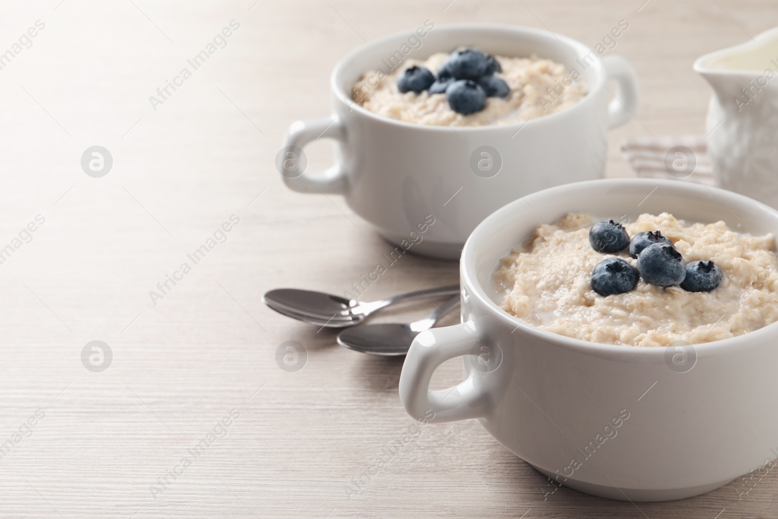 Photo of Tasty oatmeal porridge with blueberries served on light wooden table, space for text