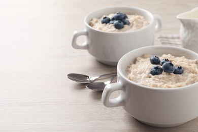 Photo of Tasty oatmeal porridge with blueberries served on light wooden table, space for text