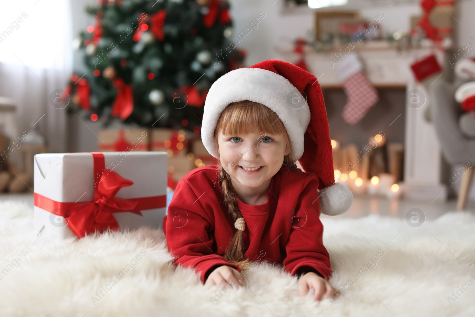 Photo of Cute little child in Santa hat with Christmas gift box at home