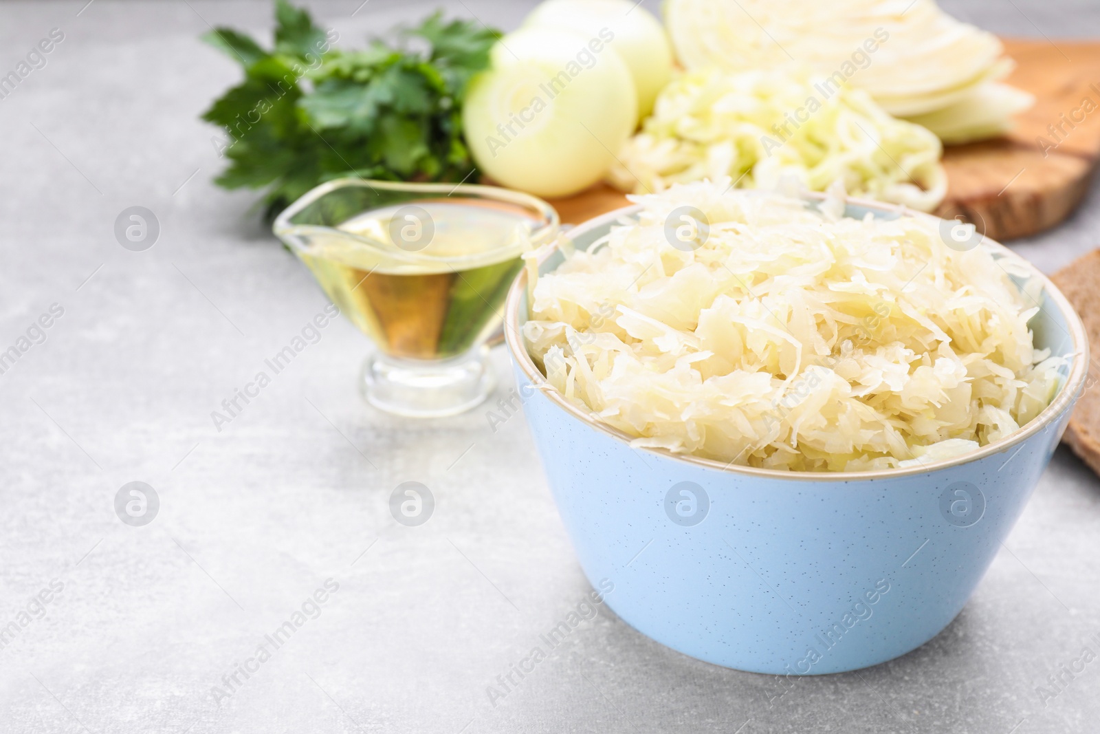 Photo of Bowl of tasty sauerkraut and ingredients on grey table, space for text