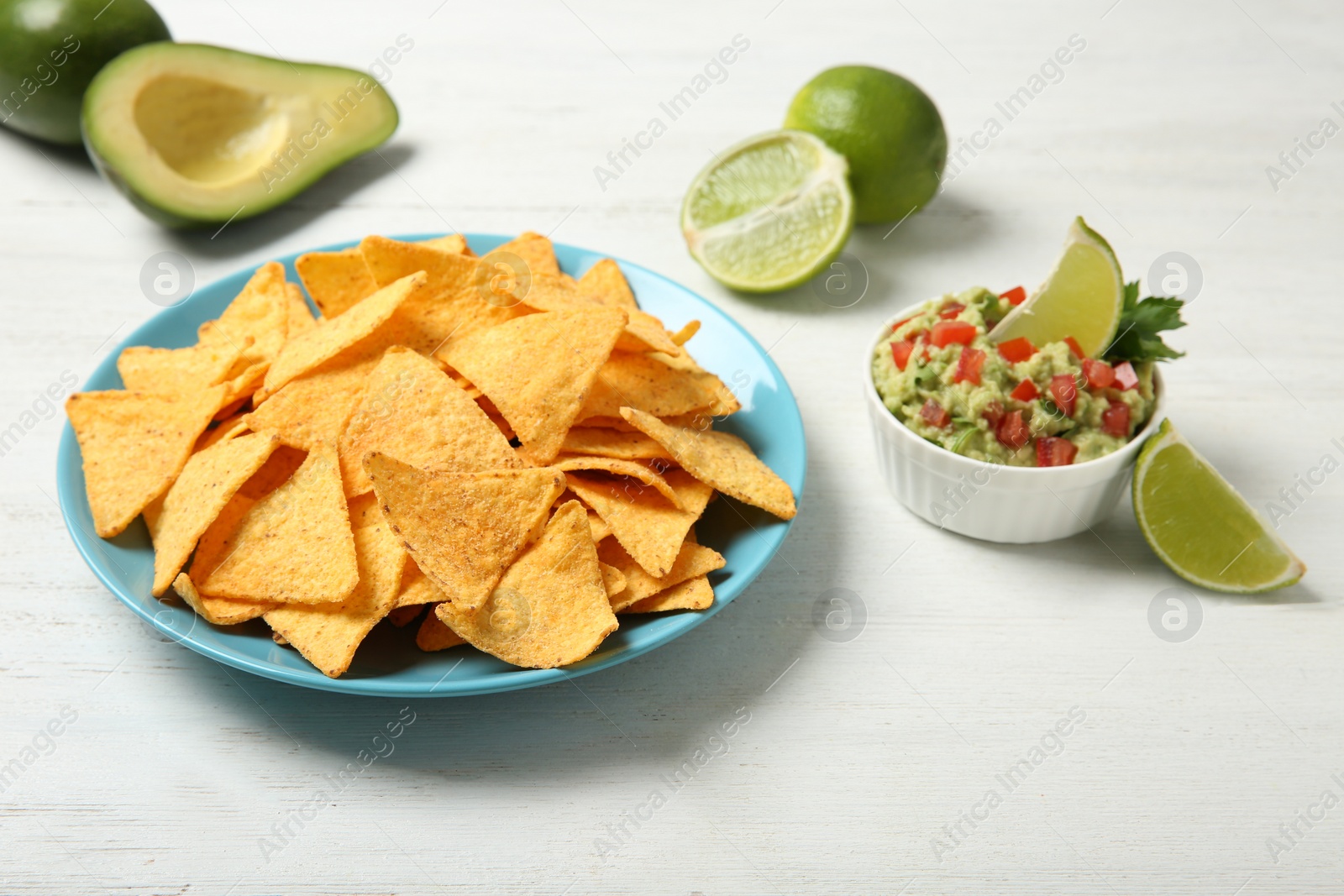 Photo of Plate with delicious mexican nachos chips, guacamole sauce and lime on white wooden table