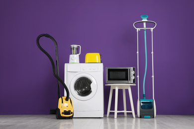 Photo of Set of different home appliances with vacuum cleaner on purple background indoors