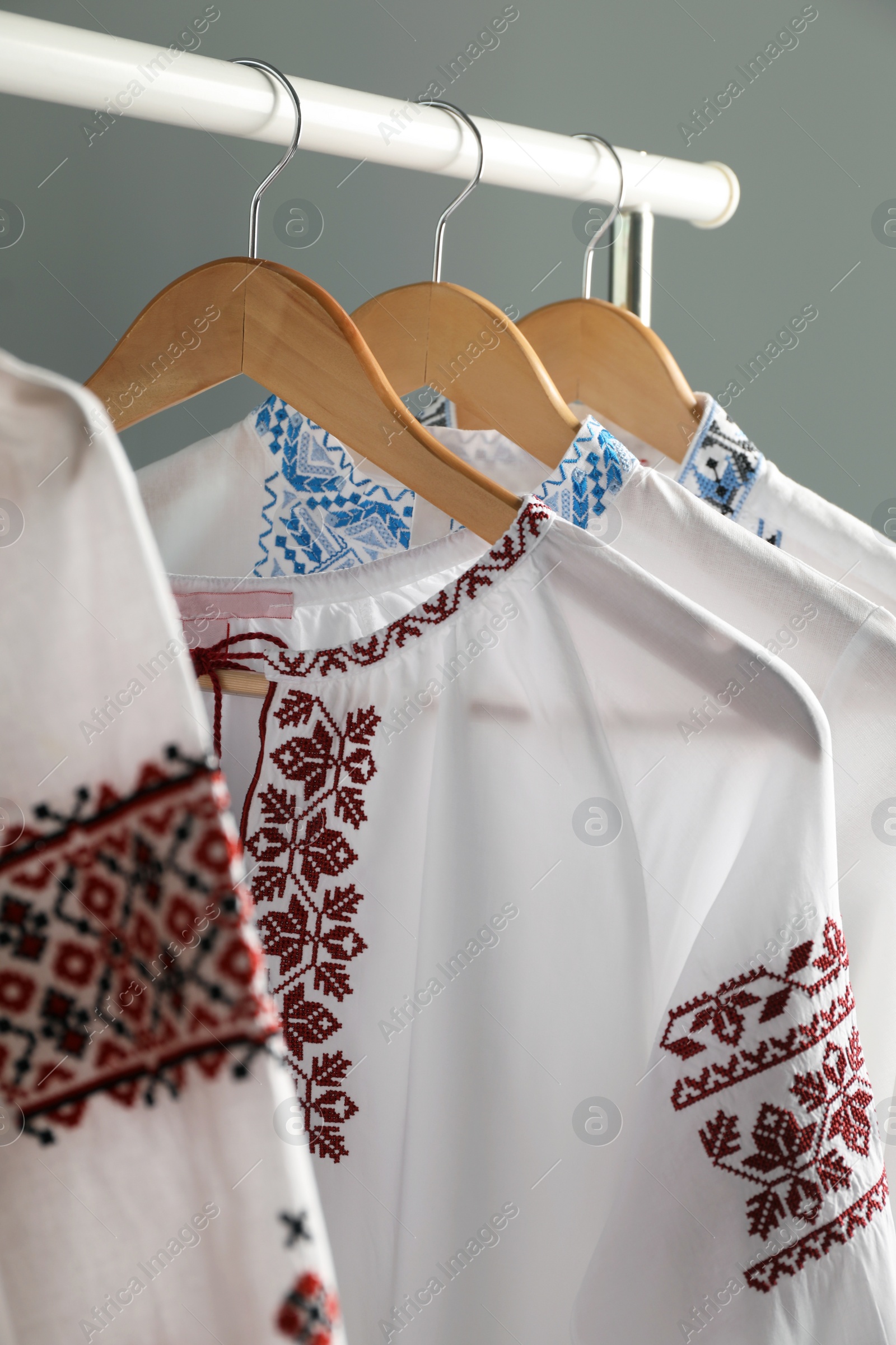 Photo of Beautiful shirts with different embroidery designs hanging on grey background, closeup. Ukrainian national clothes