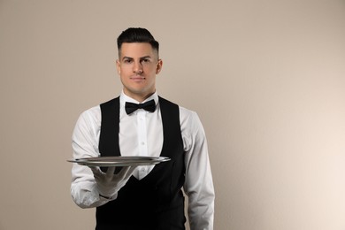 Handsome butler with tray on beige background, space for text