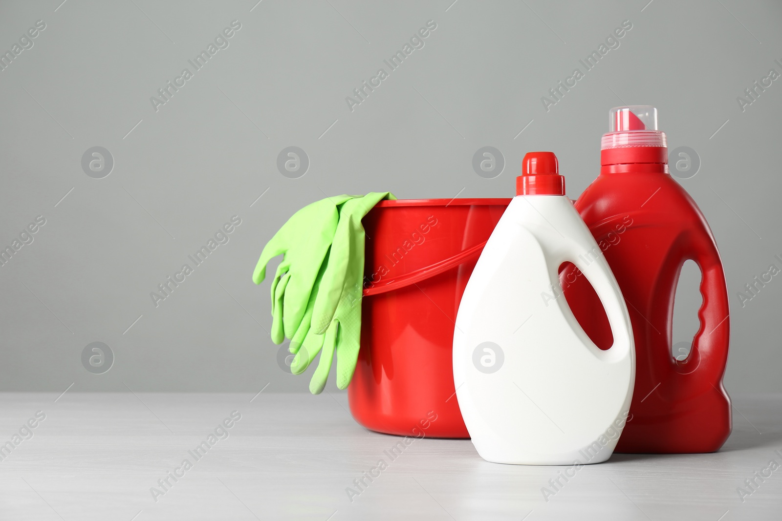 Photo of Bucket and cleaning products and gloves on grey table. Space for text