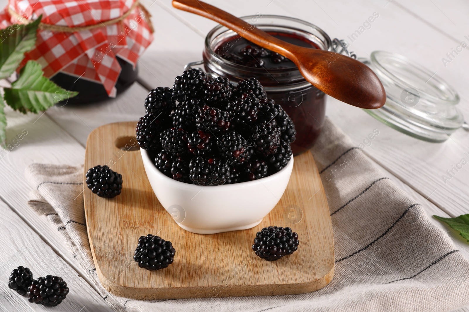 Photo of Fresh ripe blackberries and tasty jam on white wooden table