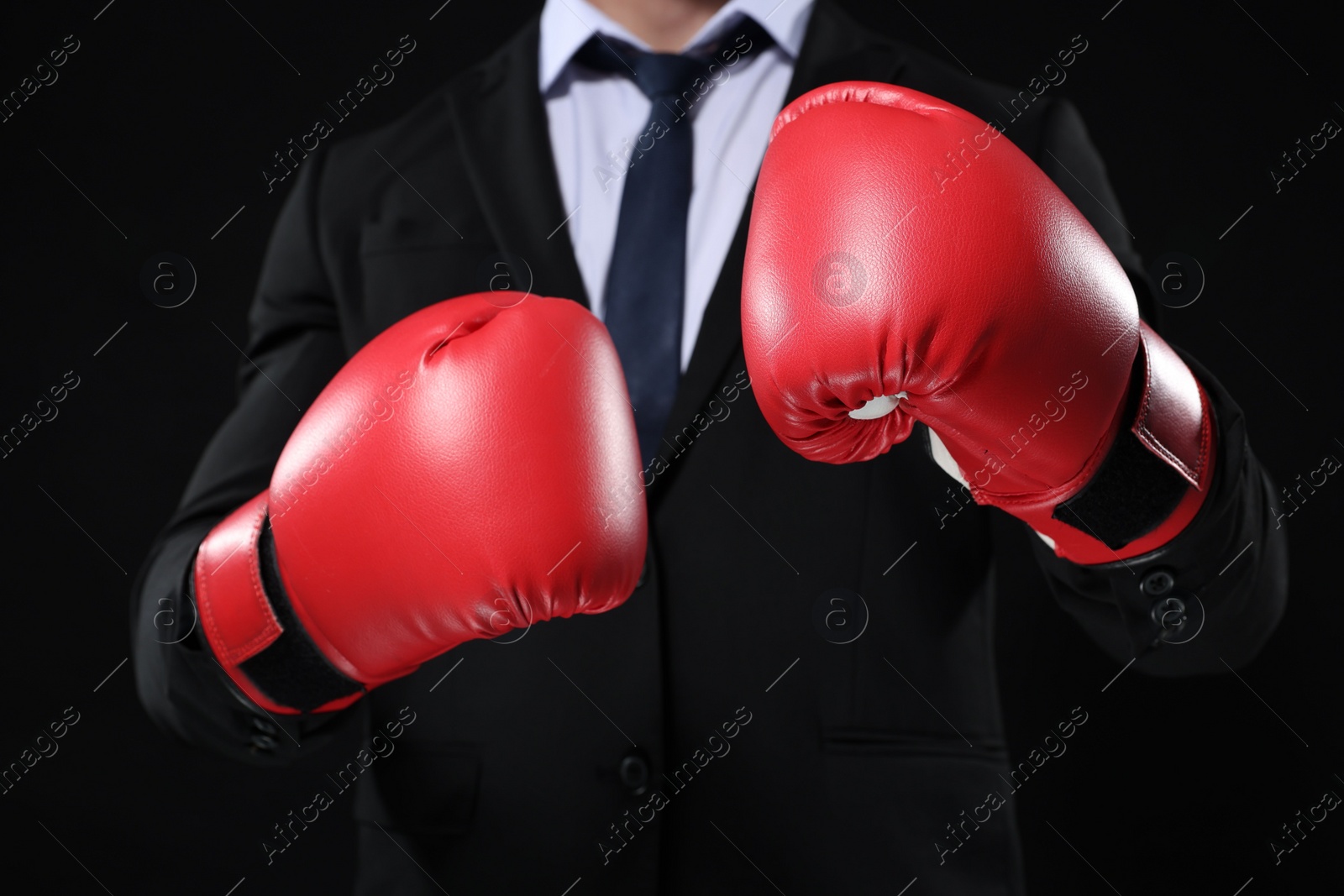 Photo of Businessman in suit wearing boxing gloves on black background, closeup